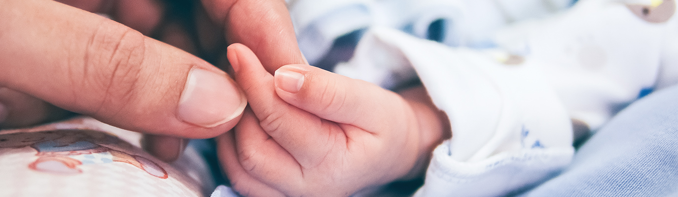 Foto van een ouderhand die een babyhandje vastpakt