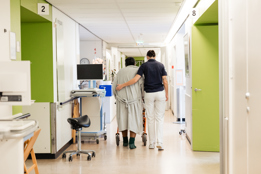 Afbeelding van een patiënt achter een rollator en een arts die een arm om haar heen slaat