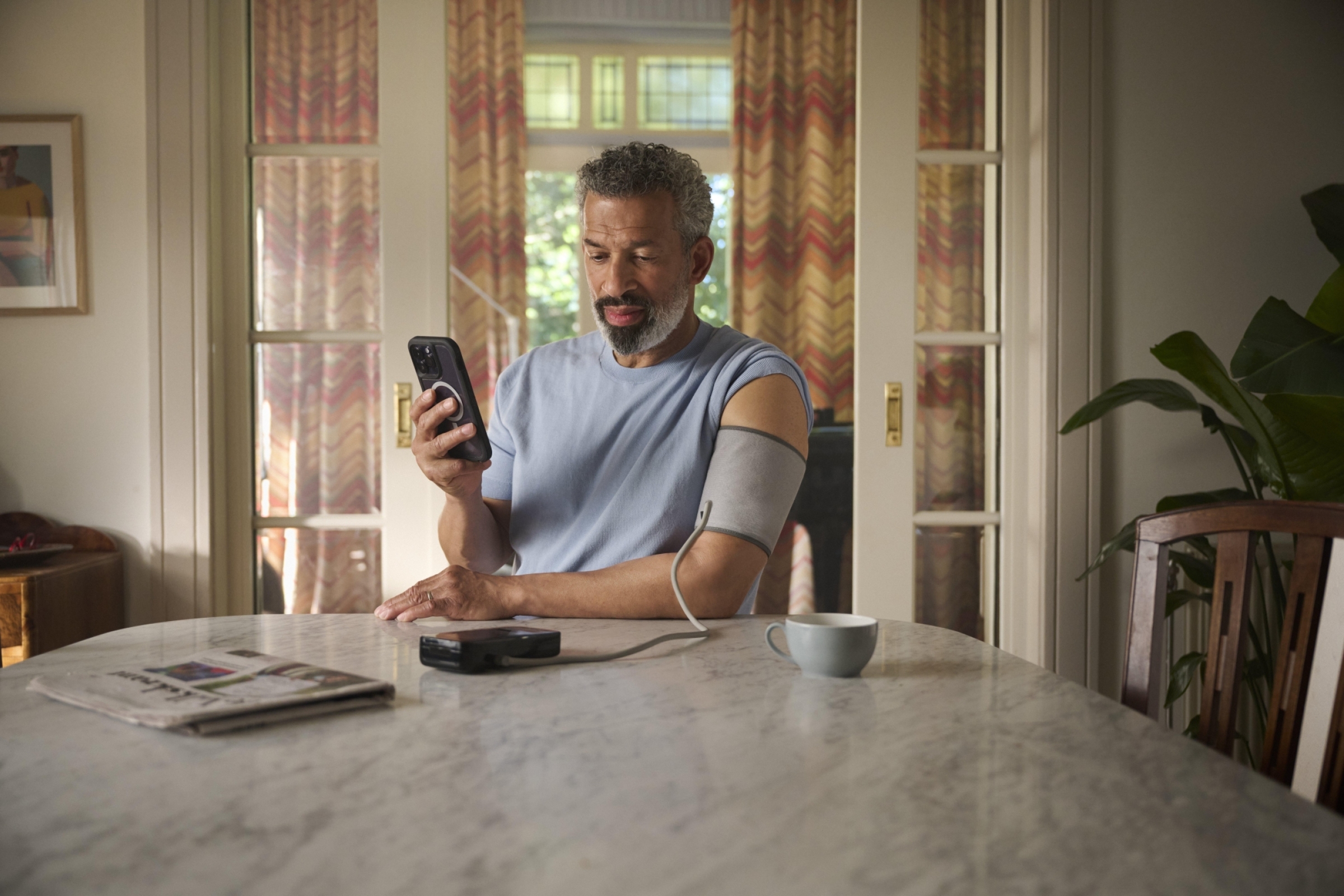 Foto van patiënt die zijn bloeddruk meet en de waarde digitaal doorgeeft via een app